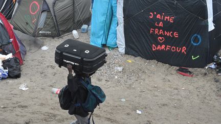 Un migrant transporte une valise au-dessus de sa tête, lundi 24 octobre 2016, alors que l'évacuation du campement de Calais débute. (FRANCOIS LO PRESTI / AFP)