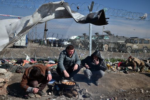 Des réfugiés font cuire des pommes de terre le long d'une clôture à la frontière gréco-macédonienne, près du village grec d'Idomeni le 19 mars 2016. (AFP - Louisa Gouliamaki)