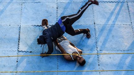 situé dans la province d'Ismaïlia, au bord du canal de Suez. Une foule de près d'un millier de personnes s'est rassemblée en ce 18 juin 2018 pour regarder ces combattants amateurs reproduire un spectacle de lutte à l'américaine. Le spectacle est une idée originale d'Ashraf Mahrous «Kabonga», qui a fondé la Fédération de lutte égyptienne en 2012. Les combattants sont encouragés par un public enthousiaste de tous âges. Sur fond de musique rock et sous des effets de lumières, ils se lancent dans un corps-à-corps qui emprunte autant à une lutte sportive qu'à une chorégraphie spectaculaire. On est loin des shows à l'américaine mais le public se régale même si ici, près d'Ismaïlia, le spectable s'arrête rapidement pour des raisons de sécurité. Si les vedettes mondiales du catch gagnent des fortunes, les amateurs égyptiens, eux, ont du mal à financer leurs spectacles et en assurer la sécurité. (MOHAMED EL-SHAHED / AFP)