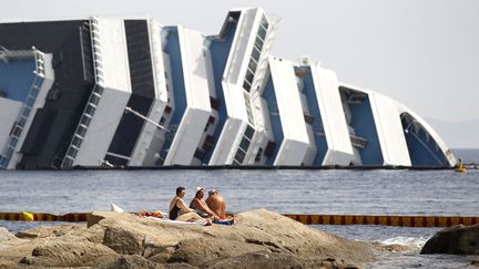 Des touristes profitent du soleil au c&ocirc;t&eacute; de l'&eacute;pave du Costa Concordia toujours &eacute;chou&eacute;e devant le port de Giglio Porto (Italie), le 20 juin 2012. (MAX ROSSI / REUTERS)