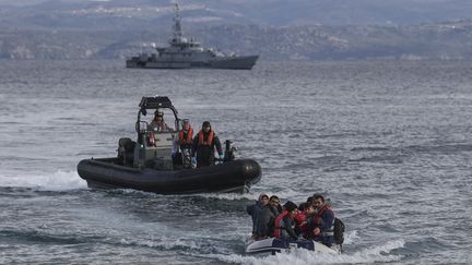 Un canot de réfugiés afghans s'approche de l'île grecque de Lesbos avec en arrière-plan un navire de patrouille de l'agence Frontex (20 février 2020).. (ARIS MESSINIS / AFP)