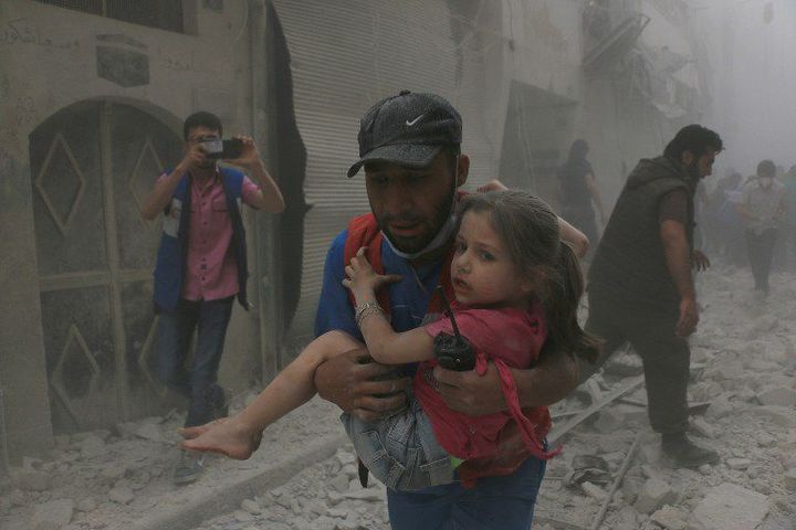 Un homme porte un enfant blessé après le bombardement d’un centre médical dans le secteur Bustan al-Kasr d'Alep, le 29 avril 2016, par des hélicoptères de l’armée syrienne. (Beha el Halebi / ANADOLU AGENCY/AFP)