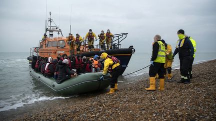 Des migrants sont aidés à débarquer d'un bateau de sauvetage de la RNLI (Royal National Lifeboat Institution) sur une plage de Dungeness&nbsp;(Royaume-Uni), le 24 novembre 2021. (BEN STANSALL / AFP)