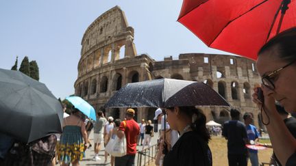 Des touristes s'abritent sous des ombrelles pendant la vague de chaleur à Rome (Italie), devant le Colisée, le 18 juillet 2023. (PABLO ESPARZA / ANADOLU AGENCY / AFP)