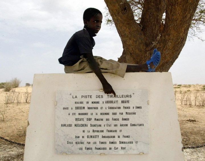 Un jeune garçon montre la plaque réalisée pour rappeler les circonstances de la réalisation d'une piste promise par la France en l'honneur du dernier tirailleur, qui habitait le village de Thiowor, au Sénégal. (SEYLLOU DIALLO / AFP)