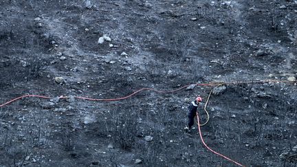 Un pompier asperge les dernières fumeroles de l'incendie de Palasca, en Haute-Corse, le 23 octobre 2017.&nbsp; (PASCAL POCHARD-CASABIANCA / AFP)