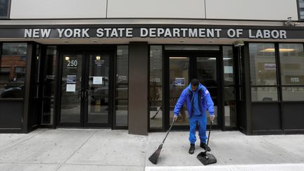 Un homme nettoie l'entrée du département du Travail de New York (Etats-Unis), le 20 mars 2020. (ANDREW KELLY / REUTERS)