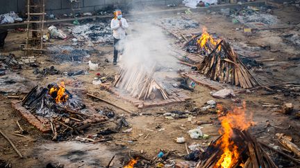 Un homme prie à côté du bûcher d'une victime décédée du Covid-19 dans un cimetière de New Delhi, le 26 avril 2021. (JEWEL SAMAD / AFP)