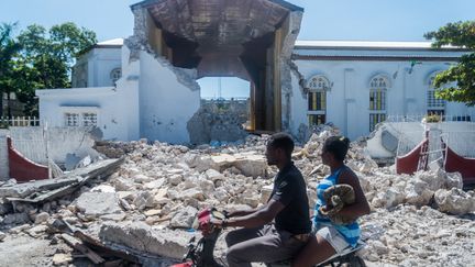 Deux personnes passent devant les ruines du Sacré coeur des Cayes dans la ville de Les Cayes en Haïti le 15 août 2021. (REGINALD LOUISSAINT JR / AFP)