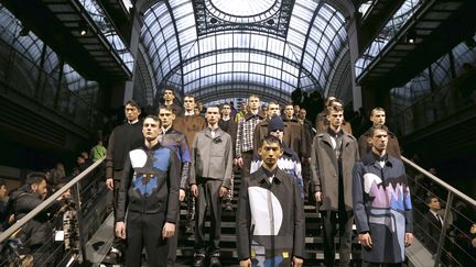 Le duo de Kenzo, Humberto Leon et Carol Lim, avait privilégié le streetwear depuis quelques saisons. Cette fois, ils mixent les styles et rendent les classiques du vestiaire masculin plus "cool" ou décontractés grâce à des éléments casuals. Ainsi, une veste de costume se ferme grâce à un zip. D'autres se portent sous un pull à capuche ou sous un blouson court, de préférence mauve pour égayer le costume gris. Les pantalons sont taille haute, près du corps et avec des pulls courts, certains à capuche. Un pantalon de costume a une poche sur le côté, à la manière du treillis. Les stylistes ont dessiné des paysages de montagne, avec neige et sapins, en blanc, mauve et bleu, sur manteaux, pulls... La collection est dominée par le marron et le gris mais du mauve et du jaune citron "boostent" l'ensemble. Sans oublier les chaussures, énormes avec de grosses semelles. Les créateurs parlent de "bottes de sécurité".
 (FRANCOIS GUILLOT / AFP)