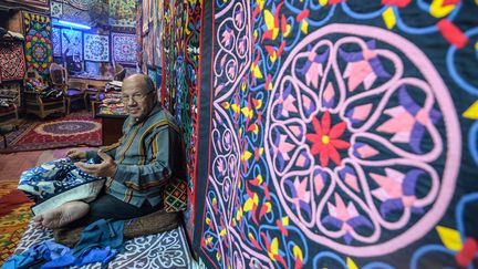 Assis en tailleur dans sa boutique du quartier historique du Caire,&nbsp;Mohsen coud à la main des pièces de tissu en coton sur des toiles aux tailles variables, à but ornemental. (MOHAMED EL-SHAHED / AFP)