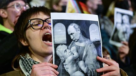 Un manifestant tient une image satirique du tableau "La Vierge à l'Enfant" de Léonard de Vinci représentant le président russe (en haut) allaitant le candidat roumain à la présidentielle, Catalin Georgescu, à Bucarest, le 25 novembre. (DANIEL MIHAILESCU / AFP)