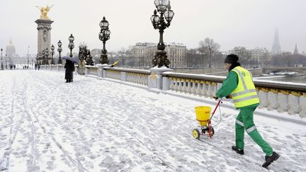 Un employé municipal déverse du sel sur le pont Alexandre III à Paris, le 2 février 2021. (STEPHANE DE SAKUTIN / AFP)