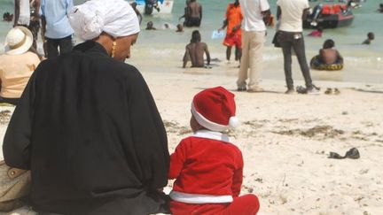 Un petit garçon déguisé en père Noël est assis, à côté de sa mère, sur la plage internationale Jomo Kenyatta à Mombasa, au Kenya, le 26 décembre 2016. 
 (ANDREW KASUKU / AFP)