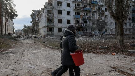 Des habitants devant un immeuble endommagé, le 2 décembre 2022 à Kluhyno-Bashkyrivka, un village dans la région de Kharkiv (Ukraine). (SOFIA BOBOK / ANADOLU AGENCY / AFP)