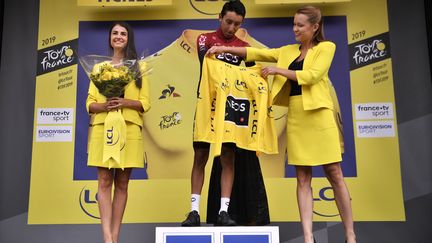 Egan Bernal (INEOS) entouré par deux "miss", sur un podium du Tour de France 2019. (MARCO BERTORELLO / AFP)