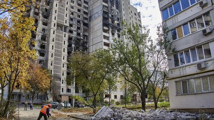 Un ouvrier ukrainien déblaie des gravats au pied d'immeubles touchés par des bombardements à Kharkiv, le 19 octobre 2022. (SERGEY KOZLOV / EPA)