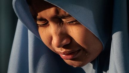 Une jeune Indonésienne, Aisha, pleure en priant avec ses parents devant la fosse commune d'Ulee Lheue, un des deux principaux sites où ont été enterrées les victimes du tsunami à Bandah Aceh (Indonésie). (YASUYOSHI CHIBA / AFP)