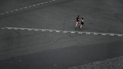 Un homme et une femme courent dans une rue déserte pendant le confinement, le 20 avril 2020. (PHILIPPE LOPEZ / AFP)