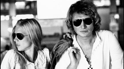 Johnny Hallyday, veste en jean sur l'épaule et croix au cou, pose avec Sylvie Vartan à MIlan en 1973. (LEEMAGE / AFP)