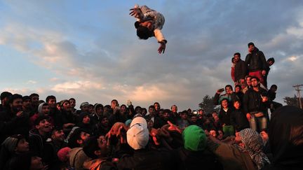 Un véritable tableau. Des réfugiés syriens dans le camp grec d'Idomeni s'offrent un moment de détente avec les moyens du bord. Ils lancent un enfant en l'air à l'aide d'une couverture. Une façon de fêter leur arrivée sur le sol européen. Depuis le 25 mars, les autorités turques bloquent les passages des réfugiés syriens vers la Grèce conformément à un accord signé avec l'Union européenne.  
 (afp/ sakis Mitrolidis - Mars 2016)