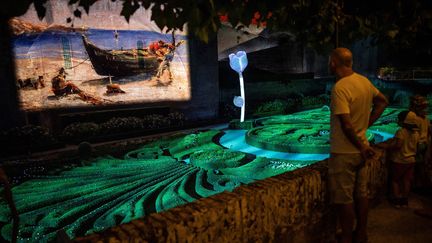 Des visiteurs regardent des projections de la vie du peintre Toulouse-Lautrec, un spectacle son et lumières de Philippe Cotten, dans les jardins du musée Toulouse-Lautrec d'Albi (France), le 18 juillet 2022. (LIONEL BONAVENTURE / AFP)