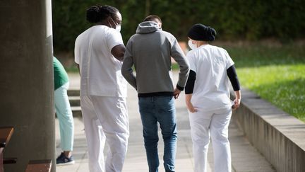 Un patient marche avec deux soignantes dans la cour du centre psychiatrique du&nbsp;Bois de Bondy (Seine-Saint-Denis), le 7 mai 2020. (LOIC VENANCE / AFP)