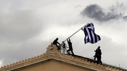 Des employ&eacute;s remplacent le drapeau sur le toit du Parlement grec, &agrave; Ath&egrave;nes, le 18 avril 2012. (YANNIS BEHRAKIS / REUTERS)