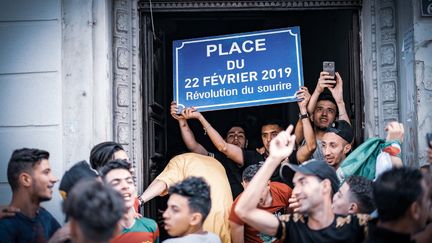 Des manifestants sous le porche d'un immeuble brandissent une pancarte "Place du 22 février 2019" à Alger, le 14 juin 2019. (SABRI BENALYCHERIF / HANS LUCAS)