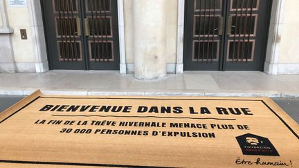 Un paillasson géant a été déroulé dimanche 31 mars par les membres de la fondation Abbé Pierre&nbsp;devant le Ministère de la Cohésion des territoires pour dénoncer les expulsions locatives.
 (MANON DERDEVET / RADIO FRANCE)