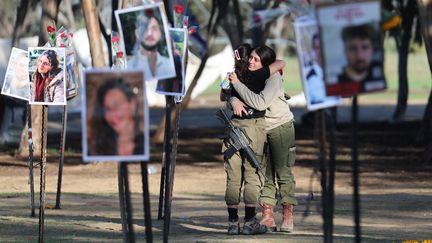 Des soldates israéliennes s'embrassent en regardant des photos des victimes du festival de musique Nova sur le site du festival, près du kibboutz Réïm (Israël), non loin de la frontière avec Gaza, le 29 novembre 2023. (ABIR SULTAN / EPA)