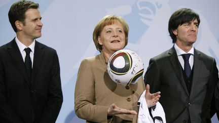 Angela Merkel joue avec un ballon aux c&ocirc;t&eacute;s du manager de l'&eacute;quipe d'Allemagne, Oliver Bierhoff (G), et du s&eacute;lectionneur Joachim L&ouml;w (D), le 10 f&eacute;vrier 2010.&nbsp; (THOMAS PETER / REUTERS)