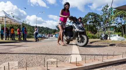 Une Guyanaise pousse son scooter sur une route bloquée par les manifestations, le 29 mars 2017, à Cayenne (Guyane).&nbsp; (JODY AMIET / AFP)