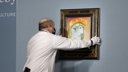 Un employé de Sotheby's prépare le tableau "Femme au béret rouge-orange" de Pablo Picasso au Bellagio, le 23 octobre 2021 à Las Vegas&nbsp;(Etats-Unis). (GABE GINSBERG / GETTY IMAGES NORTH AMERICA / AFP)