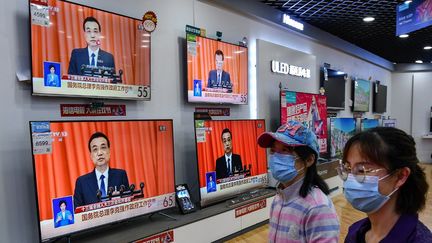 Des habitants de Pékin écoutent le discours du&nbsp;Premier ministre chinois, Li Keqiang, le 22 mai 2020, à l'ouverture de la session annuelle de l'Assemblée nationale populaire. (STR / AFP)