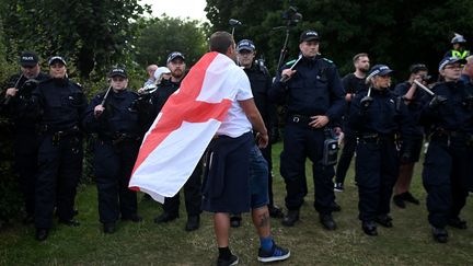 Un manifestant portant un drapeau de Saint-Georges se tient devant une file de policiers à Bristol, dans le sud de l'Angleterre, le 3 août 2024, lors de la manifestation  après les agressions au couteau mortelles à Southport le 29 juillet. (JUSTIN TALLIS / AFP)