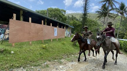 Des habitants de la tribu de Tiendanite, à Hienghène (Nouvelle-Calédonie), passent à cheval devant les panneaux électoraux installés pour le référendum, le 1er décembre 2021. (RAPHAEL GODET / FRANCEINFO)