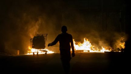 Une personne marche près d'une barricade en feu sur une route à du Lamentin (Martinique), le 1er décembre 2021, après plus d'une semaine de manifestations violentes déclenchées par les restrictions&nbsp;contre le Covid-19.&nbsp; (ALAIN JOCARD / AFP)