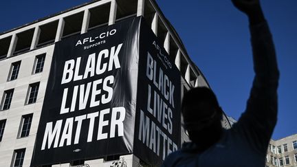 Devant un immense panneau "Black Lives Matters", un homme lève le poing&nbsp;à Washington. (ANDREW CABALLERO-REYNOLDS / AFP)