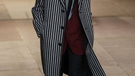 Dimanche soir, juste avant le lancement de la haute couture printemps-été 2014, Saint Laurent a clôturé les défilés de mode masculine avec une collection plus sage mais qui garde des inspirations rock. Premier look, un pantalon noir, près du corps, court, avec une veste grise assez longue. Une écharpe est enroulée négligemment autour du cou du mannequin qui porte une gros manteau gris. Plusieurs looks assez sages se succèdent. Depuis qu'Hedi Slimane créé pour Saint Laurent, il a misé sur le grunge et le rock. Le designer retravaille des incontournables de la garde-robe masculine dont le costume. Puis des perfecto, des carreaux rouges et noirs, des blousons rouges avec du léopard, du cuir se mélangent à ce vestiaire. Une chemise à jabot se porte avec une veste rose brillante. Certains looks font penser aux années 50 plus qu'aux eighties. Cette garde-robe est toujours réservée aux hommes très minces. Pour Pierre Bergé, l'ancien compagnon d'Yves Saint-Laurent, "c'est la meilleure collection d'Hedi chez Saint Laurent. C'est formidable. Magnifique". Pour François-Henri Pinault, Le PDG de Kering, propriétaire de Saint Laurent, "c'est un nouveau répertoire, mais avec la même inspiration, qui dépasse les codes établis. C'est une vision très rock n'roll de la vie".
 (FRANCOIS GUILLOT / AFP)