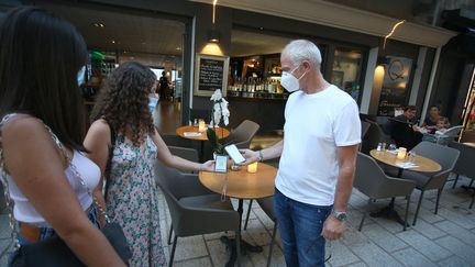 Un restaurateur vérifie le pass sanitaire d'une cliente à la terrasse d'un restaurant à l'Île-Rousse (Haute-Corse), le 23 juillet 2021. (PASCAL POCHARD-CASABIANCA / AFP)