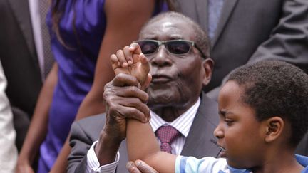 Le pr&eacute;sident zimbabw&eacute;en Robert Mugabe essaie de forcer &agrave; chanter le petit-fils d'un de ses vice-pr&eacute;sidents lors d'une c&eacute;r&eacute;monie &agrave; Harare (Zimbabwe), le 12 d&eacute;cembre 2014. (TSVANGIRAYI MUKWAZHI / AP / SIPA)