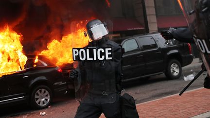 Un policier américain devant une limousine incendiée à Washington (Etats-Unis) en marge de l'investiture de Donald Trump, le 20 janvier 2017. (SPENCER PLATT / GETTY IMAGES NORTH AMERICA / AFP)