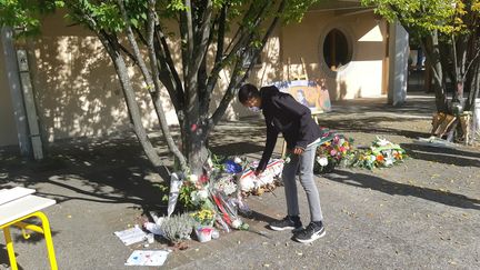 Un élève dépose une fleur lors de la cérémonie d'hommage à Samuel Paty, au collège du Bois d'Aulne à Conflans (Yvelines), où le professeur enseignait, le 16 octobre 2021. (GILLES GALLINARO / RADIO FRANCE)