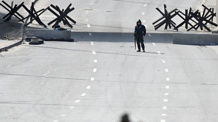 Un soldat ukrainien armé surveille un checkpoint à l'entrée de Kiev, en mars 2022. (SERGEI SUPINSKY / AFP)