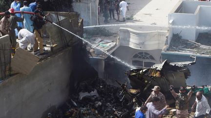 Des policiers utilisent des lances à eau après le crash d'un avion de la Pakistan International Airlines dans un quartier résidentiel de Karachi, vendredi 22 mai 2020. (ASIF HASSAN / AFP)