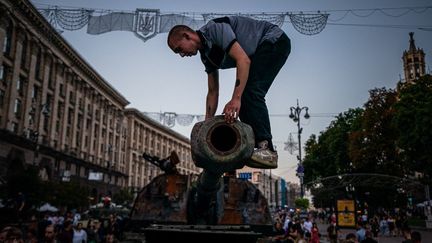 Un&nbsp;homme grimpe sur un char d'assaut russe détruit dans une rue de&nbsp;Kiev, le 21 août 2022, qui a été transformée en musée militaire en plein air à l'approche de la fête de l'indépendance de l'Ukraine le 24 août.&nbsp; (DIMITAR DILKOFF / AFP)