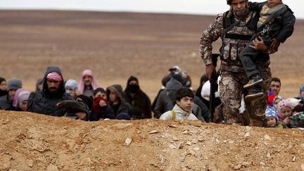 Un soldat jordanien porte un jeune r&eacute;fugi&eacute; syrien qui vient de traverser la fronti&egrave;re pr&egrave;s de&nbsp;Ruwaished (Jordanie), le 5 d&eacute;cembre 2013. (MUHAMMAD HAMED / REUTERS)