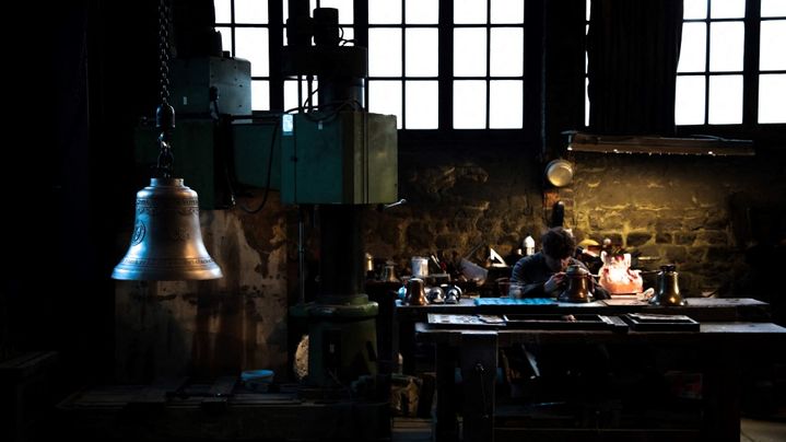 Un employé travaille à côté d'une cloche, à la fonderie Cornille Havard de Villedieu-les-Poêles, le 5 décembre 2022. (LOU BENOIST / AFP)