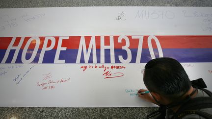 Un Malaisien signe une banderole sur laquelle est &eacute;crit "Espoir MH370", &agrave; S&eacute;pang, en Malaisie, dimanche 16 mars 2014.&nbsp; (EYEPRESSNEWS / AFP)